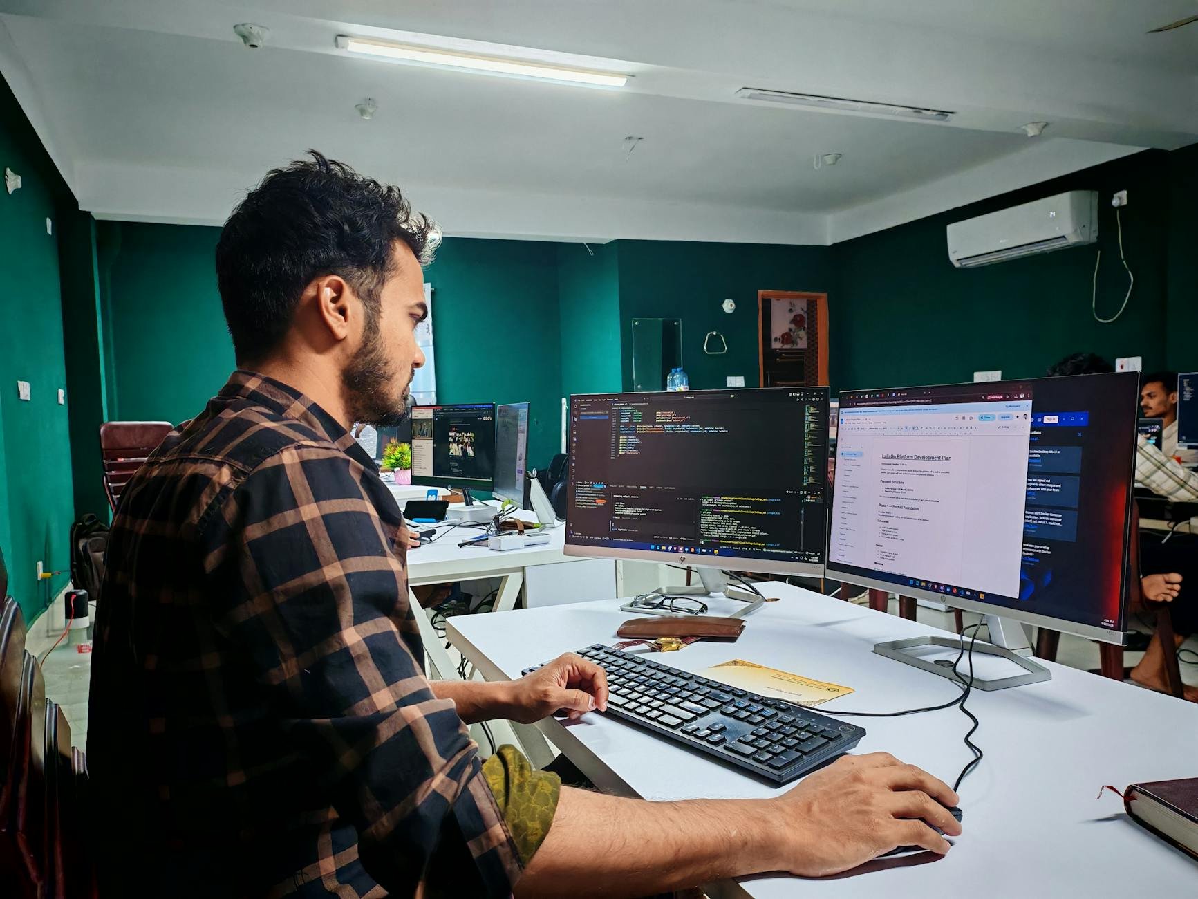 Software developer coding on dual monitors in a modern, well-lit office.